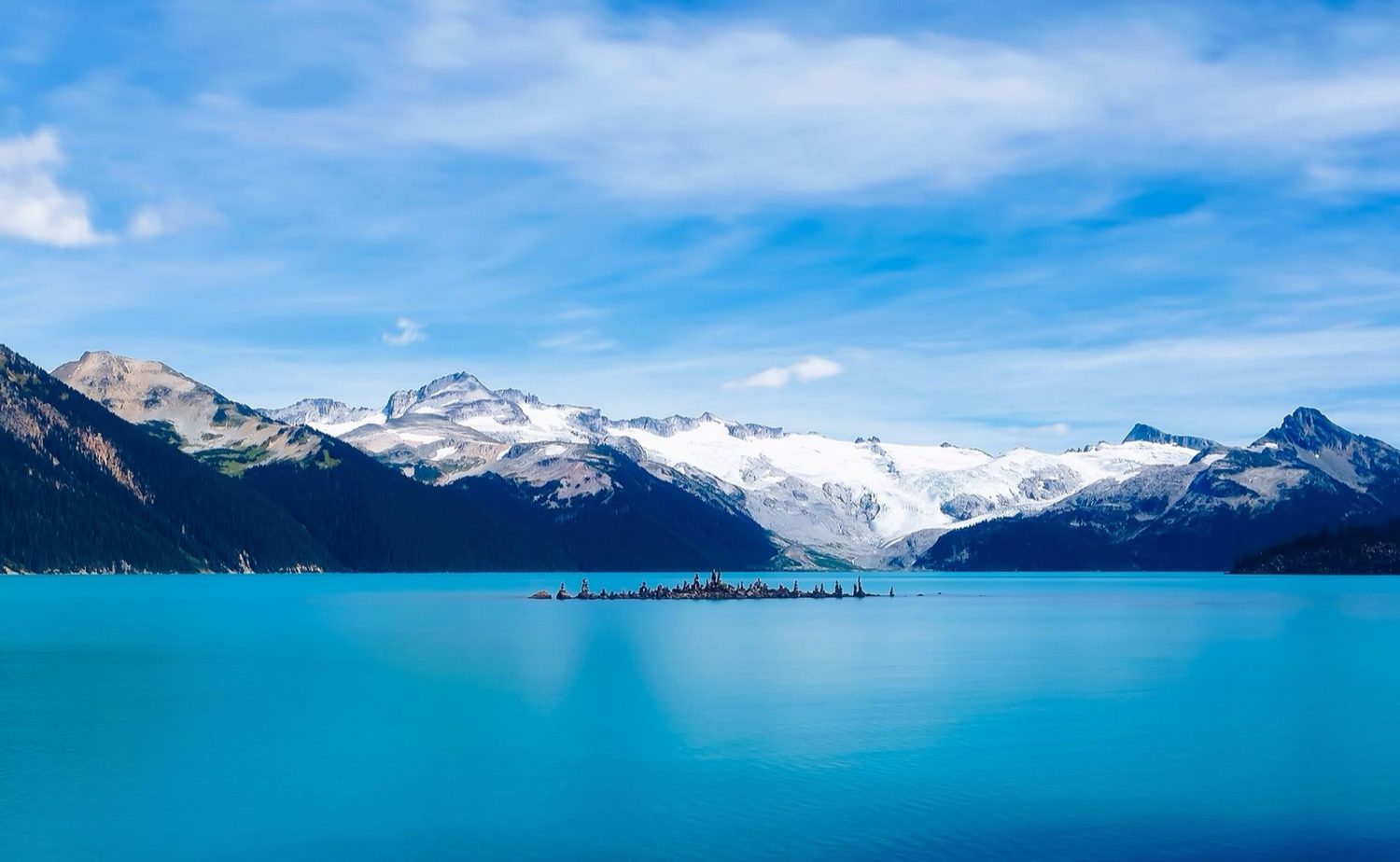 A turquoise alpine lake below snow-streaked mountains