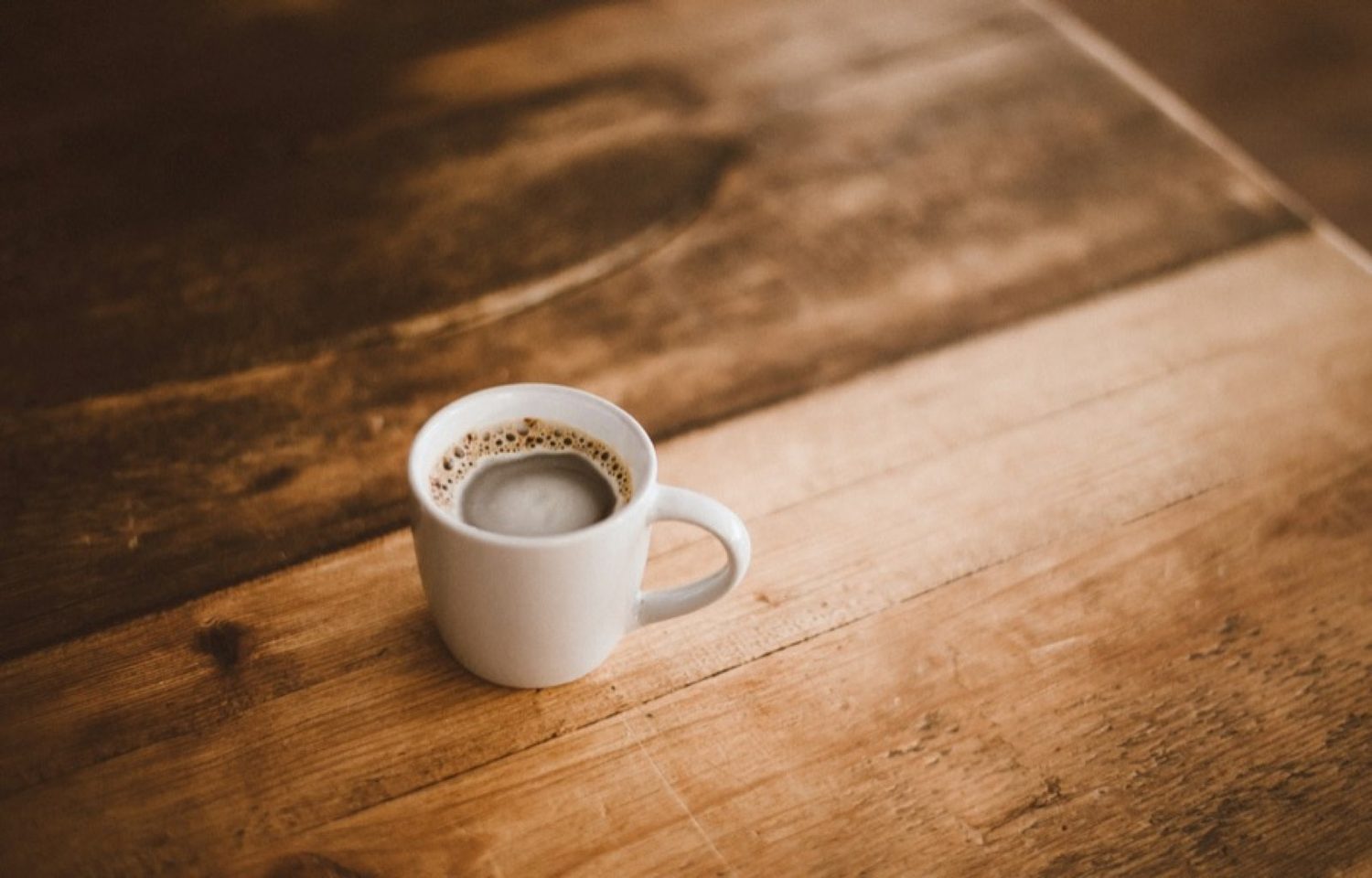 A white mug of coffee on a worn wooden table