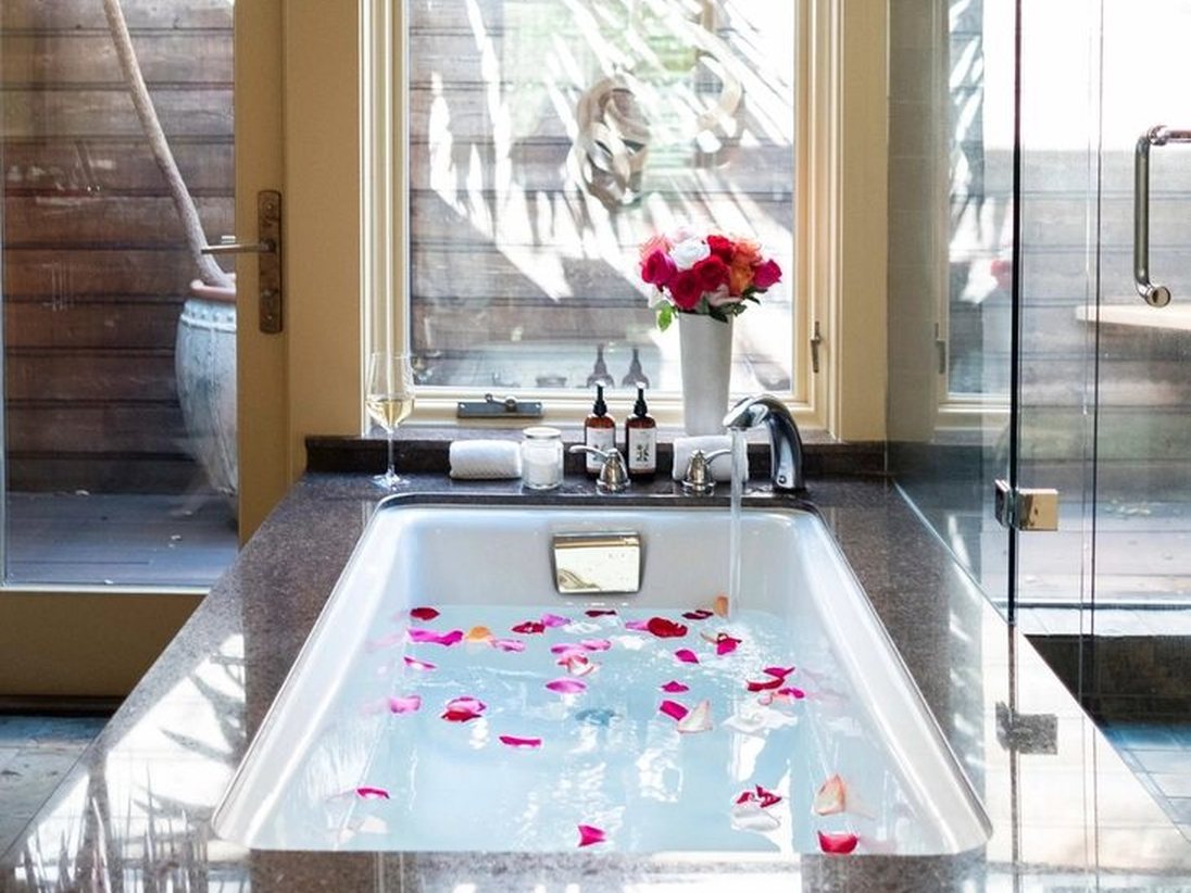 A deep jacuzzi bathtub set in tile, dressed with petals and a bottle beside it