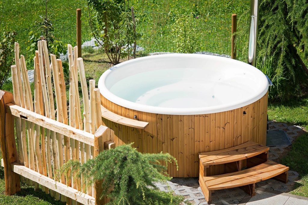 A round wooden hot tub with a step, set in a garden