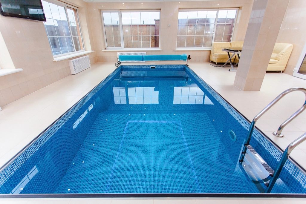 A bright indoor swimming pool with tall windows along one side