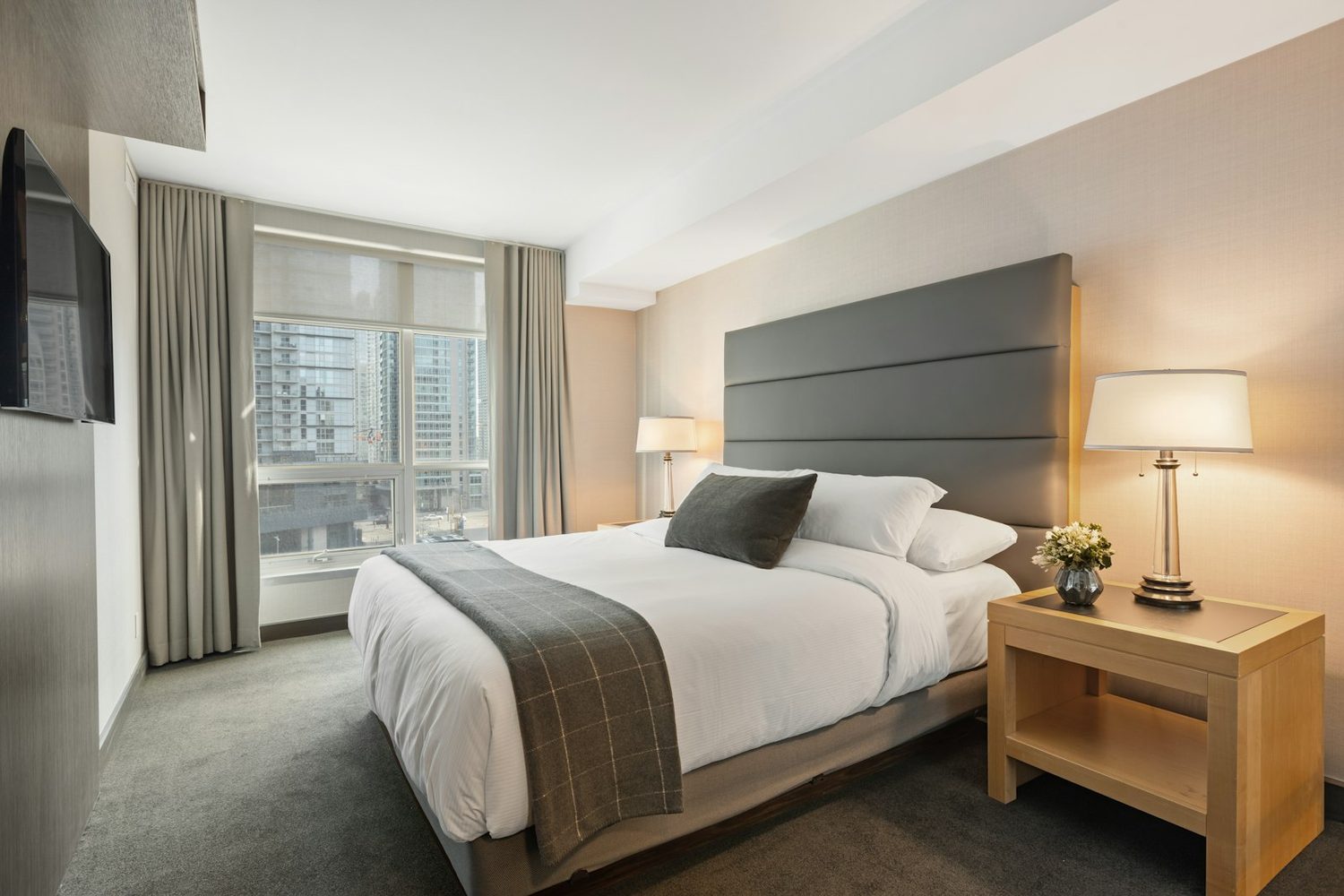 Spacious guest room with a king bed, upholstered headboard and a wall-mounted flat screen