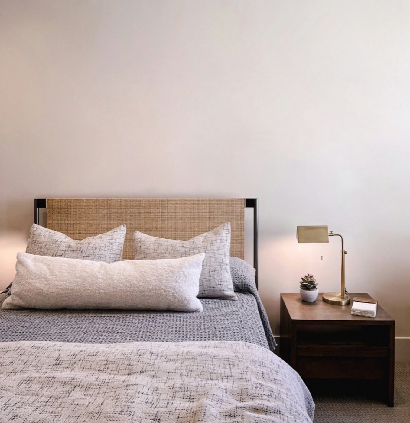 Calm bedroom with a cane headboard, layered bedding and a warm bedside lamp